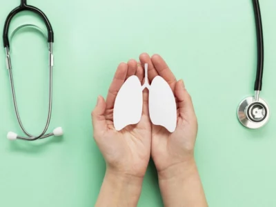 Hands holding lungs cutout with stethoscope on green background