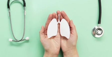Hands holding lungs cutout with stethoscope on green background